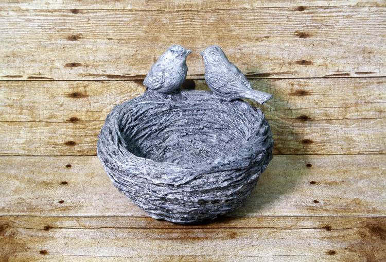 An image of a planter in the shape of a nest with two birds perched upon the edge.